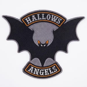 May include: A black and gray embroidered patch featuring a stylized bat with wings spread wide. The text HALLOWS is arched across the top in white letters with an orange border, and the word ANGELS is arched across the bottom in white.