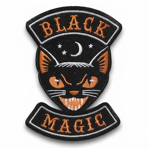 Op de afbeelding: Een zwarte geborduurde patch met een gestileerd kattengezicht met oranje ogen en oren, witte snorharen en scherpe tanden. Boven de kat staan een witte maansikkel en drie sterren. De tekst BLACK MAGIC is in het oranje geborduurd op gebogen banen.