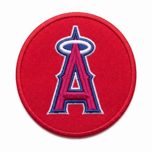 May include: A circular embroidered patch featuring a bright red background. Centered on the patch is a stylized letter A in pink, outlined in dark blue and white, topped with a white halo with a blue border, all rendered in dense thread.