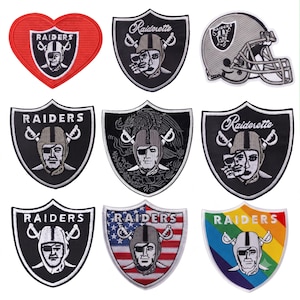 Op de afbeelding: Een verzameling van negen geborduurde patches met het Raiders-logo, in schild- en hartvormen. De ontwerpen tonen de klassieke piratenmascotte met een ooglapje, gekruiste zwaarden en variaties met de Amerikaanse vlag en een regenboogachtergrond.