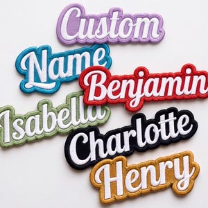 Könnte beinhalten: Eine Sammlung von sechs bestickten Namensaufnähern mit weißer Schreibschrift auf farbigem Hintergrund. Die Aufnäher zeigen die Wörter Custom, Name, Benjamin, Isabella, Charlotte und Henry in den Farben Lila, Blau, Rot, Grün, Schwarz und Gold.