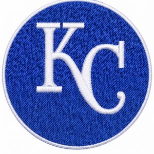 May include: A circular embroidered patch featuring a royal blue background with a white border. Centered on the patch are the white embroidered letters Kc in a stylized serif font. The texture of the embroidery is visible throughout the design.