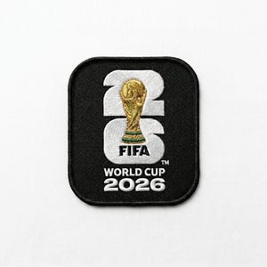 Könnte beinhalten: Ein quadratischer, schwarzer Stickaufnäher mit abgerundeten Ecken, der den weißen Text 26 und das Logo der FIFA World Cup 2026 zeigt. Das zentrale Design enthält ein goldenes Pokalsymbol zwischen den Zahlen sowie den Text FIFA World Cup 2026 darunter.