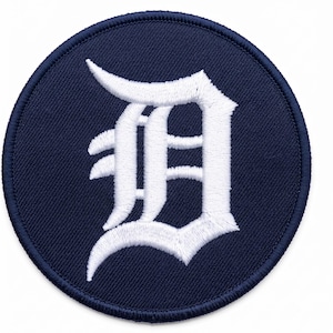 Op de afbeelding: Een ronde geborduurde patch met een donkerblauwe achtergrond en een wit geborduurde gotische letter D in het midden. De patch is voorzien van een dikke, donkerblauwe festonsteekrand die de ronde vorm van het ontwerp omlijst.