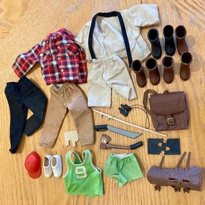 May include: A collection of miniature doll clothing and accessories, including a red and black plaid shirt, brown boots, a green tank top with the number 9, and a brown backpack. Other items include pants, shorts, and a toy axe.
