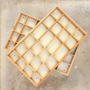 May include: Two rectangular wooden display trays with multiple square compartments. Each tray features a light-colored natural wood frame and a white base, with small circular holes visible in the bottom of several individual sections.