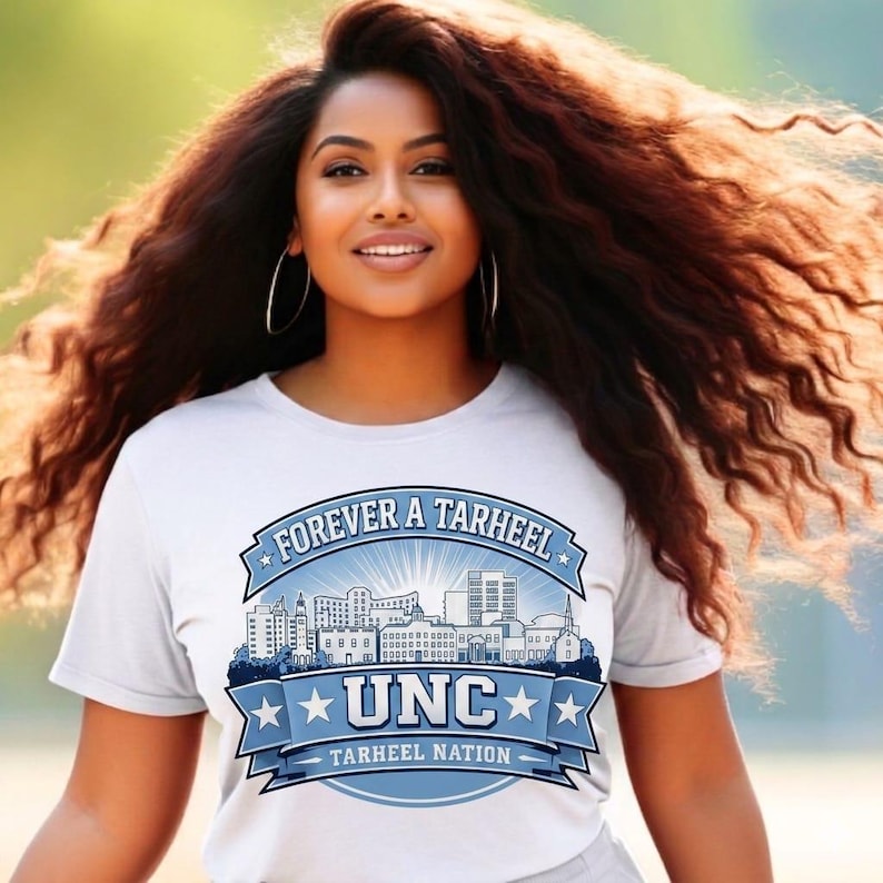 May include: A white t-shirt with the text "FOREVER A TARHEEL" and "UNC TARHEEL NATION" in blue. The design includes a cityscape and stars. The shirt is worn by a person with long, wavy brown hair.