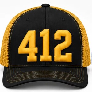 May include: A black baseball cap with a yellow mesh back and a yellow embroidered number 412 on the front. The cap features a structured crown, a curved brim with yellow stitching, and a button on top, showcasing a bold color contrast design.