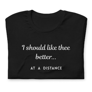 Może przedstawiać: Czarny t-shirt z białym napisem "I should like thee better... AT A DISTANCE". Złożona koszulka ukazuje dekolt i tekst w swobodnej czcionce. Koszulka wykonana jest z miękkiego materiału.