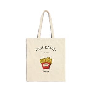 Pode incluir: Saco tote creme com o texto "GIGI DAVID EST. 2025" acima de um gráfico de batatas fritas num recipiente vermelho. A palavra "forever" está abaixo das batatas fritas. O saco tem duas alças.