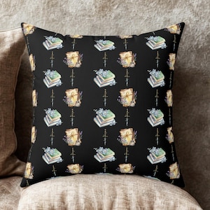 Op de afbeelding: Zwart decoratief sierkussen met een herhalend patroon van aquarel illustraties. Het patroon bevat stapels boeken, rollen, bloemen en dolken. Het kussen is vierkant en heeft een zachte, uitnodigende uitstraling.