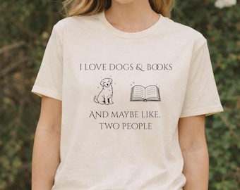 May include: Cream-colored t-shirt with the text "I LOVE DOGS & BOOKS" above a dog and book illustration. Below the illustration, the text reads "AND MAYBE LIKE, TWO PEOPLE". The shirt is made of a soft material.