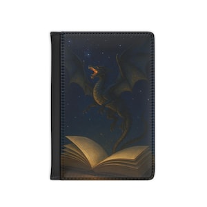 Puede incluir: Un tarjetero de pasaporte de cuero negro con una ilustración de fantasía. Un dragón con las alas extendidas vuela sobre un libro abierto contra un cielo estrellado. La boca del dragón está abierta y las páginas del libro brillan.