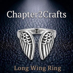 Puede incluir: Un anillo plateado con un diseño abierto, con motivos de alas detallados en cada lado. El anillo está estampado con "925" y los textos "Chapter2Crafts" y "Long Wing Ring" se muestran arriba y abajo del anillo.