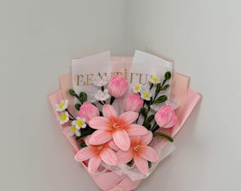 May include: A bouquet of handmade pink flowers, including lilies and tulips, wrapped in pink paper and tied with a white ribbon. The bouquet includes small white and yellow flowers. The words "BEAUTIFUL" are printed on the paper.