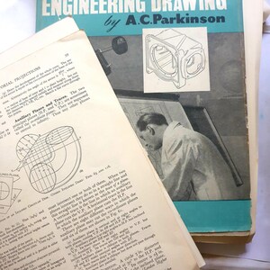 May include: An old textbook titled "Intermediate Engineering Drawing by A.C. Parkinson" with diagrams and text. Another book with text is partially visible, along with a drawing.