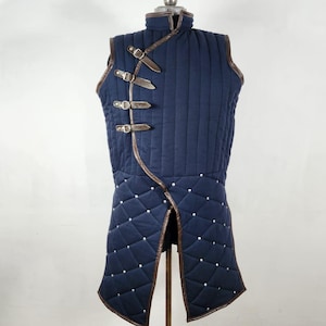 May include: A navy blue quilted vest with brown leather trim and accents. The vest features a high collar, diamond stitching, and three leather straps with buckles on the front. The bottom hem has a split design.