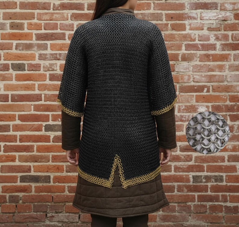 May include: A black chainmail shirt with short sleeves and gold trim. It is worn over a brown padded gambeson. A close-up of the chainmail is in the lower right corner. The background is a brick wall.