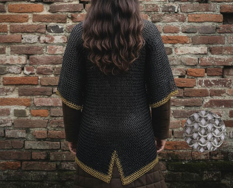 May include: Black chainmail shirt with gold trim on the sleeves and hem. The shirt is worn over a brown long-sleeved garment. The background is a weathered brick wall. A close-up of the chainmail is in the lower right corner.