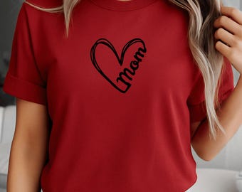May include: A red t-shirt featuring a black heart with the word "Mom" written inside. The shirt has short sleeves and a crew neck. The design is simple and elegant, suitable for everyday wear.