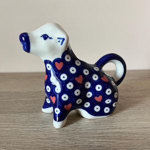 Könnte beinhalten: Keramikhundefigur mit blau-weißem Tupfenmuster und roten Herzakzenten. Der Hund hat einen weißen Kopf und Beine, mit einer blauen Nase und einem blauen Schwanz. Die Figur ist ein dekorativer Artikel.