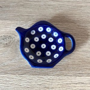 Könnte beinhalten: Ein kobaltblauer Keramik-Teebeutelhalter in Form einer Teekanne. Der Halter hat ein Muster aus weißen Punkten und einen kleinen Griff. Der Teebeutelhalter ist zum Auffangen von Tropfen gedacht.
