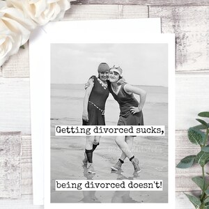 May include: Black and white photo of two women in vintage swimsuits standing on a beach. The text "Getting divorced sucks, being divorced doesn't!" is printed below the photo.