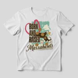 May include: White t-shirt with a graphic design. The design features the text "BORN AND RAISED Massachusetts" in a vintage style, along with illustrations of cookies, a coffee cup, and a star. The shirt is made of a soft material.