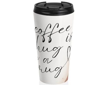 May include: White travel mug with a black lid. The mug has the handwritten text "coffee is a hug in a mug" in black script. The mug is designed to keep drinks warm or cold.