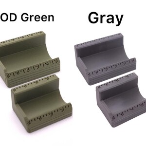 May include: Two small, curved, rectangular holders, one in OD green and the other in gray. Each has a ruler-like marking along the top and bottom edges. The text "OD Green" and "Gray" are above the respective holders.