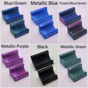 May include: A collection of 3D-printed card holders in various colors, including blue/green, metallic blue, purple/blue/green, metallic purple, black, and metallic green. Each holder has a curved design and a ruler-like detail along the top edge.