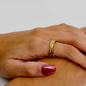 May include: A tri-color ring featuring three interlocking bands in yellow, rose, and white metal tones. The design consists of smooth, polished surfaces that overlap to create a continuous, intertwined structure worn on a finger.