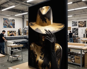May include: A framed artwork featuring a person with gold paint and a gold hat. The person's face is partially obscured by a black gloved hand. The hat is gold with black accents. The artwork is displayed in a workshop.