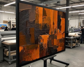 May include: Large abstract painting with a black frame. The artwork features textured brushstrokes in shades of orange, brown, and black. The painting is displayed on a wheeled stand in a workshop setting.