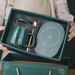 May include: A teal mug set with a warming plate, lid, and gold spoon, presented in a teal gift box. The mug has the word "lucky" printed on it. The set is designed for keeping beverages warm.