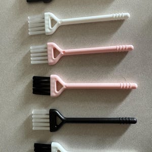 May include: A set of six cleaning brushes with triangular heads and long handles. The brushes feature various color combinations: black handle with black bristles, white handle with white bristles, pink handle with white bristles, pink handle with black bristles, black handle with white bristles, and white handle with black bristles.