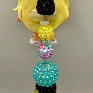 May include: A decorative pen featuring a yellow character design with a black beaded pen barrel. The pen is adorned with various colorful beads, including black, yellow, pink, and turquoise, and a light blue wing-shaped accent.