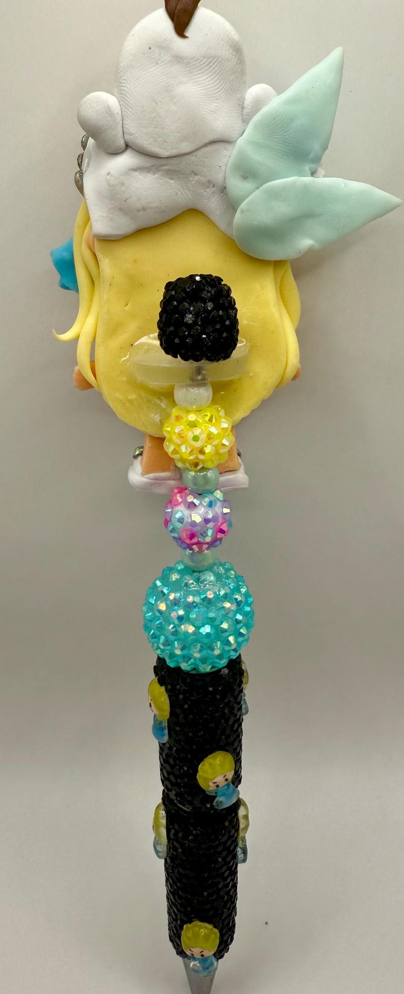 May include: A decorative pen featuring a yellow character design with a black beaded pen barrel. The pen is adorned with various colorful beads, including black, yellow, pink, and turquoise, and a light blue wing-shaped accent.