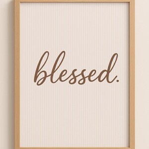 Puede incluir: Una impresión enmarcada con la palabra "blessed" en escritura marrón. El fondo es de color beige claro con líneas verticales. El marco es de madera de color claro.
