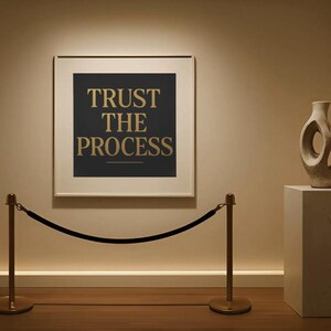Puede incluir: Una escena de galería de arte con una obra de arte enmarcada con el texto "TRUST THE PROCESS" en letras doradas sobre un fondo oscuro. Un jarrón decorativo se encuentra sobre un pedestal. Una barrera de cuerda de terciopelo está en primer plano.