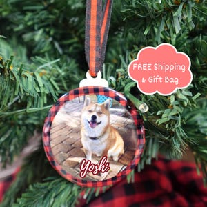 K&ouml;nnte beinhalten: Eine runde Weihnachtskugel mit einem Foto eines Hundes namens Yoshi. Die Verzierung hat einen rot-schwarz karierten Rand und ein schwarz-orange gestreiftes Band zum Aufh&auml;ngen. Der Hund ist hellbraun und wei&szlig;.
