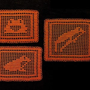 May include: Three orange crocheted rectangular placemats with scalloped edges. Each mat features a different design: a fish, a lightning bolt, and a whale. The mats are set against a black background.