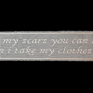 May include: A rectangular, off-white, crocheted piece with the text "all my scars you can see when I take my clothes off" in white letters. The piece has a decorative, scalloped edge and is set against a black background.