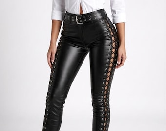 May include: A white button-down shirt paired with black leather pants featuring lace-up detailing along the sides. The outfit is completed with a black belt and pointed-toe high-heeled boots.