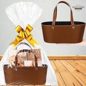 May include: A brown leather gift basket with a matching handle, presented in cellophane and tied with a gold bow. The basket is filled with gifts, and another basket is shown separately. The Trendy Leather logo is visible.
