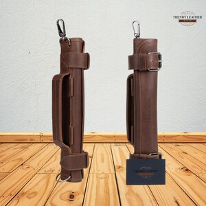 May include: Two brown leather cases with silver-tone hardware. Each case has a handle, a buckle, and a strap. The cases are standing on a wooden surface. The cases have the text "TRENDY LEATHER GIFTS" on them.