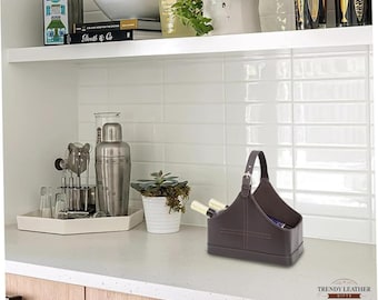 May include: A brown leather wine bottle carrier with a handle and buckle, holding two bottles. The carrier is on a countertop with a white tile backsplash. The words "TRENDY LEATHER GIFTS" are in the bottom right corner.