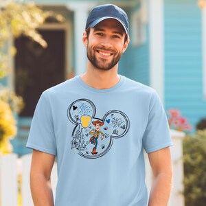 A smiling man wearing a blue baseball cap and a light blue t-shirt with a Mickey Mouse design.