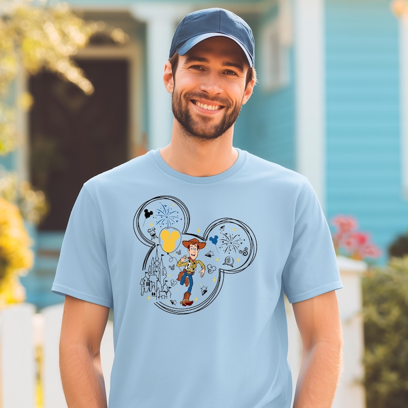 A smiling man wearing a blue baseball cap and a light blue t-shirt with a Mickey Mouse design.