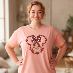 A woman wearing a pink t-shirt with a cartoon character and a bow on it, smiling at the camera.